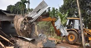 Assam Evictions - This image shows a straw sculpture displayed during Bhogali Bihu celebrations in Assam, India, in 2021. The sculpture is crafted to resemble a "Corona Hospital," reflecting the impact of the COVID-19 pandemic on society. The intricate structure includes a thatched building with a "Corona Hospital" sign, an ambulance marked "108," and straw figures symbolizin